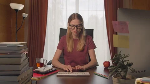 Young girl at computer table, typing on keyboard, looking at camera, calling on Video stock 132891352
