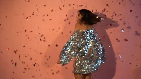 Young girl dancing and having fun in the rain of confetti on a pink background Stock Footage 143736945