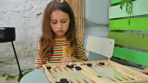 Young girl deeply focused on playing backgammon outdoors Stock Footage 290053540