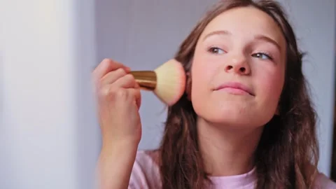Young girl demonstrating makeup application techniques in a well-lit indoor Stock Footage 310506705