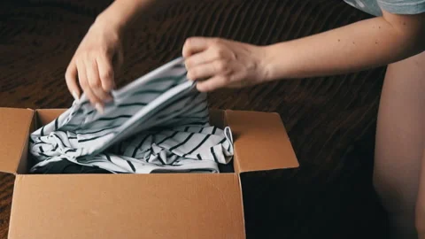 Young Girl Disassembles a Parcel With Things and Examines Clothes Stock Footage 198143216