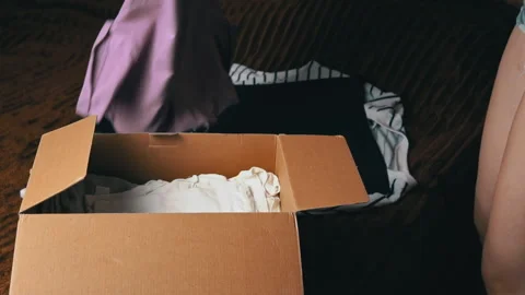 Young Girl Disassembles a Parcel With Things and Examines Clothes Stockbeeldmateriaal 199010098