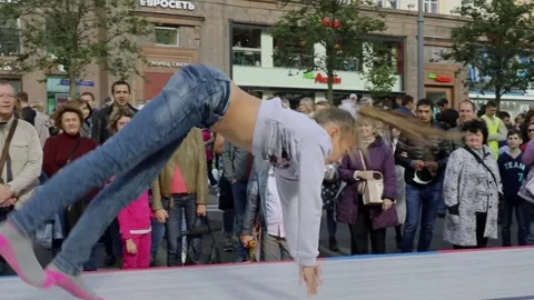 Young girl does acrobatic jump sequence among crowd of people during City Day Stock Footage 276377326
