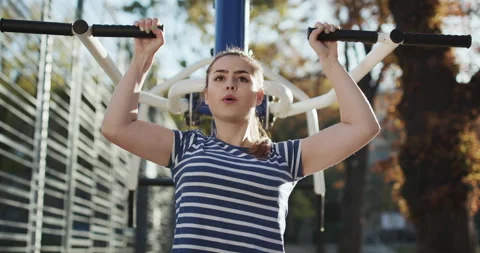 Young girl does chin-up exercise on sports ground in autumn park. Attractive Stock Footage 195260650