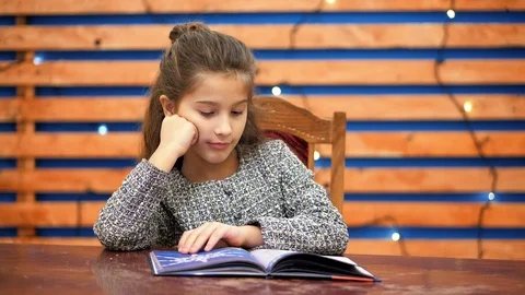 A young girl does homework, leafs through pages of a book.The girl is peeped out Stock Footage 120268812