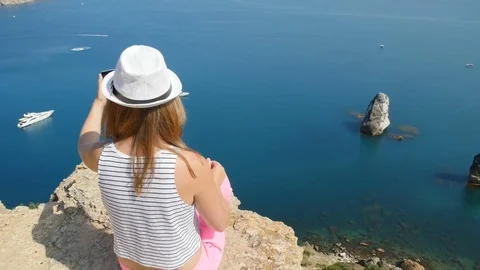 A young girl does selfie next to the blue sea sitting on a mountain Video stock 80659112