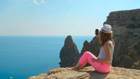 A young girl does selfie next to the blue sea sitting on a mountain Stock Footage 80659715