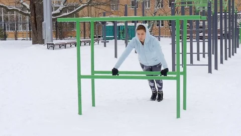 Young girl doing push-ups on the bars. Fitness Workout Outdoors Winter Stock Footage 69814778