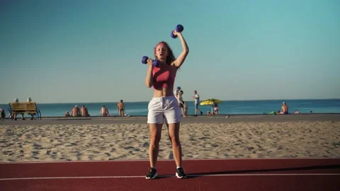 Young girl doing training with weight on the street, pressing dumbbells up,  Stock Footage 198885617