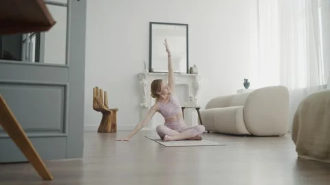 Young girl is doing yoga sitting on rug in bright studio. Yoga exercises. Yoga Stock Footage 242291153