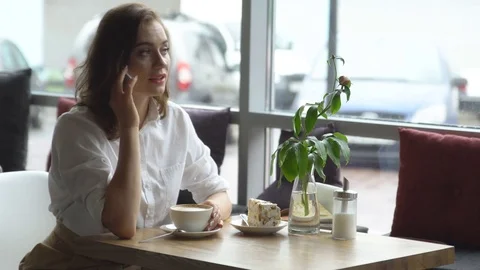 Young girl drinking coffee and talking on mobile phone in cafe. business woman Stock Footage
