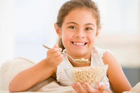 Young girl eating cereal in living room smiling Stock Photos