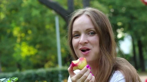 A young girl eats an apple, laughing, outdoors. Stock Footage 80091834