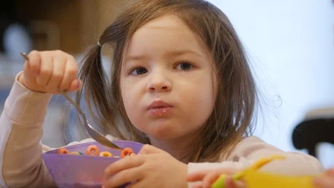 Young girl eats cereal at kitchen counter looking toward the camera chewing 스톡 동영상 86713437