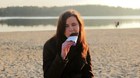 Young girl eats chocolate at river bank Video stock 64299629
