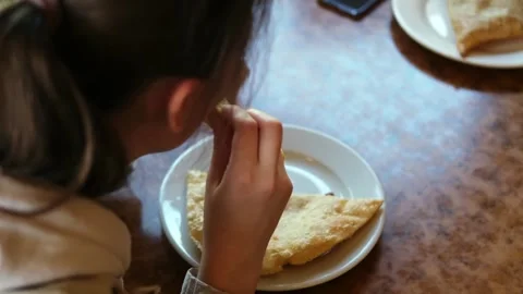 A young girl eats a fried cheburek pie sitting at a table in a cafe. Stock Footage 282168494