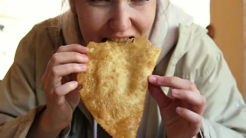 A young girl eats a fried cheburek pie sitting at a table in a cafe. Stock Footage 282168496
