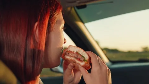 Young girl eats hamburger while sitting car seat, girl face touches hamburger Stock Footage 258731709