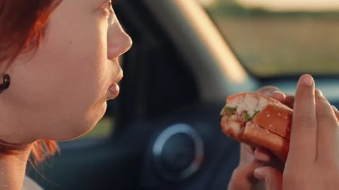 Young girl eats hamburger while sitting car seat, girl face touches hamburger Stock Footage 258986457