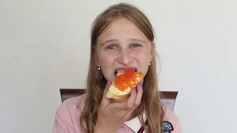 Young girl eats a sandwich with bread, butter and red caviar Stock Footage