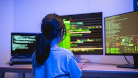 Young Girl Engaged in Coding Activity in a Dark Room with Multiple Computer.. 写真素材