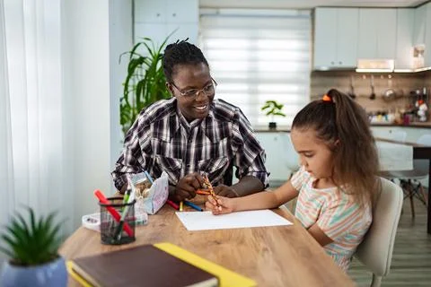 A young girl engaged in learning while an adult helps her with schoolwork. Stock Photos