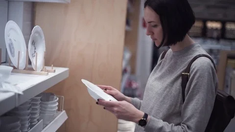 Young girl examining plates in the section of dishware in housewares store Stock Footage 83433154