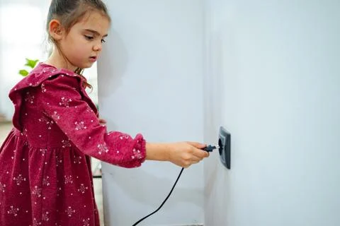 Young girl exploring electricity by plugging in a device in a cozy indoor space Stock Photos