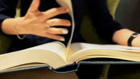 Young girl flips a page while reading a book in a university Stock Footage 114293296