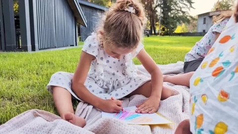 A young girl is focused on coloring with crayons while sitting on a blanket. She Stock Footage 341490959