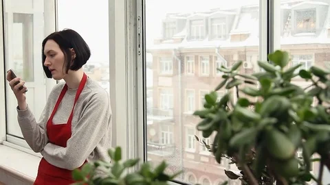 Young girl gardener in red apron chatting online using smartphone in greenhouse Video stock 87730053