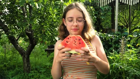 Young girl in glasses eats a watermelon in the garden Stock Footage 114106963