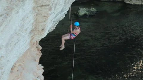 Young Girl goes Down From The a Steep Rock With a Rope Against the Sea Video stock 59451586