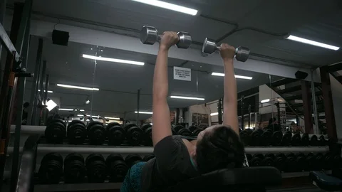 Young girl in great shape doing dumbbell lifts on a lying bench in the gym Stock Footage 89498467