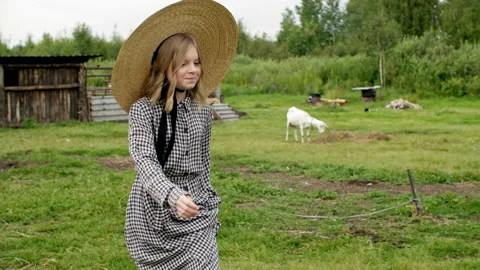 Young girl in hat walking on rural barnyard. Rustic girl walking on livestock in Stock Footage 140480341