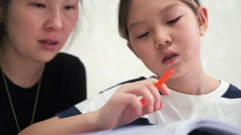 Young girl hesitates while solving task with pencil near lips as mother Stock Footage 333483656