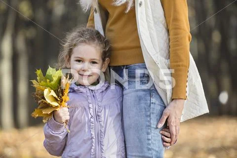 A young girl holding a bouquet of autumn leaves and holding onto her Mom Stock Photos
