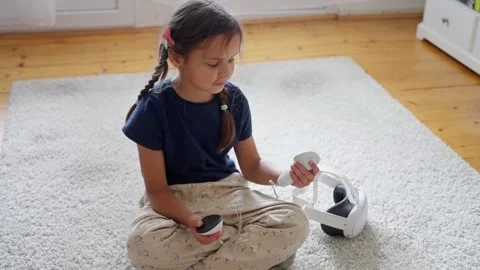 A young girl interacts with VR controllers, exploring the world of virtual Stock Footage 317757920