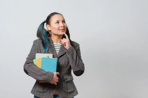 A young girl in a jacket with a stack of books in her hands. gaze directed at Stock Photos