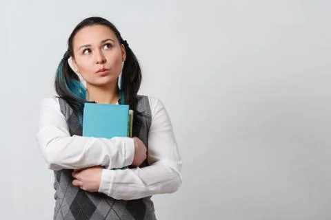 A young girl in a jacket with a stack of books in her hands. gaze directed at Stock Photos