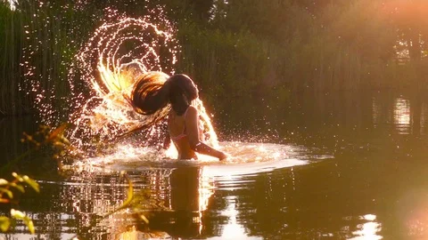 Young girl jump up from lake making fan splash with her hair slow motion Stock Footage