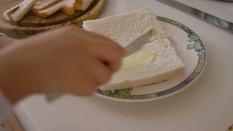 Young girl in the kitchen buttering bread as she prepares to make a sandwich Video stock 127871013