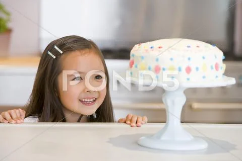 Young girl at kitchen counter looking at cake smiling Stock Photos