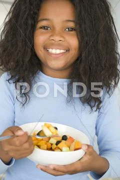 Young girl in kitchen eating bowl of fruit smiling Stock Photos