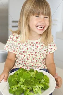 Young girl in kitchen eating broccoli smiling Stock-Fotos