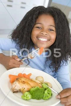 Young girl in kitchen eating chicken and vegetables smiling Stock Photos
