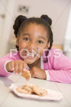 Young girl in kitchen eating cookies smiling Stock-Fotos