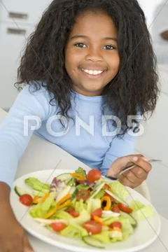 Young girl in kitchen eating salad smiling Stock Photos