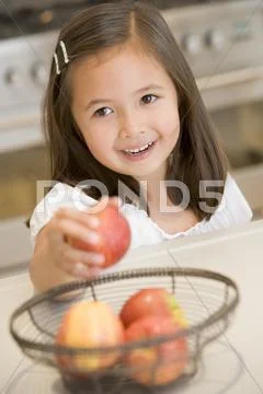 Young girl in kitchen getting apple off counter smiling Stock-Fotos