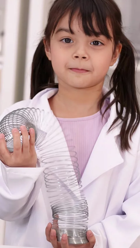 Young Girl in Lab Coat Playing with Metal Spring Toy Stock Footage 344105053